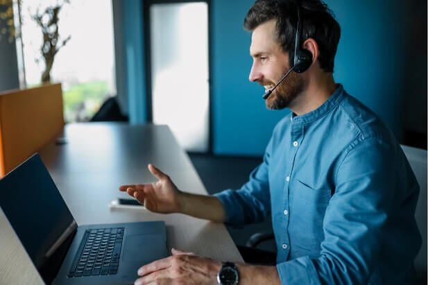 Man with headset smiling and looking at laptop